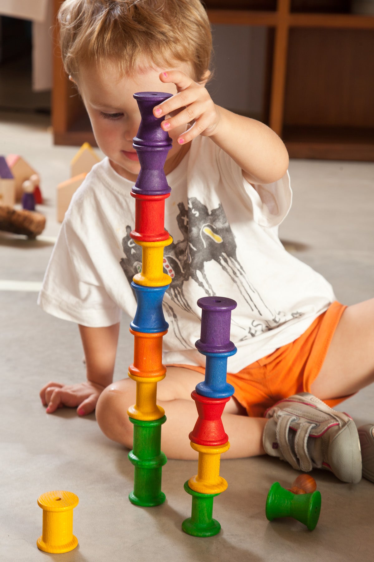 a small child plays with rainbow coloured wooden spools.  They are stacking the spools in two towers,